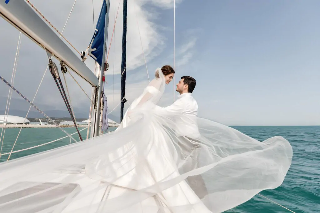 The bride with a huge veil and the groom pose on a yacht in the middle of the sea The bride and groom on a yacht