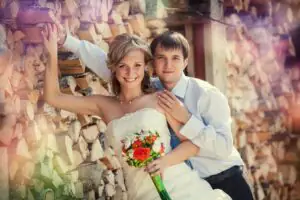 The bride and groom pose against a wall of wooden logs The wedding couple