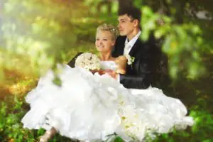 The bride and groom pose sitting under a tree on the grass The bride and groom are sitting