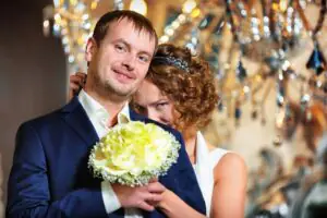 The bride hides her face behind the groom, who is holding a wedding bouquet Newlyweds with a wedding bouquet