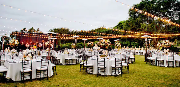 The tables are set in the open air, with garlands hanging over them Tables set on the green grass