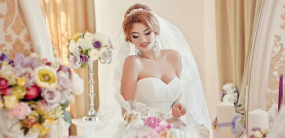 A bride in a long veil poses among bouquets of flowers The bride in a long veil