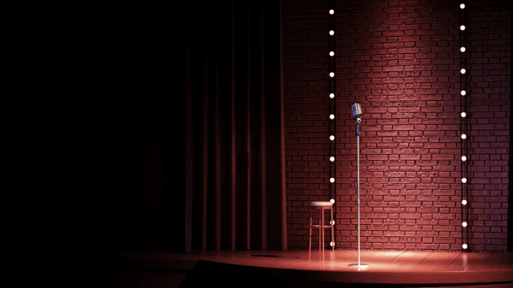 A stage for stand-up comedians with a chair and a microphone on the stand A chair and a microphone stand on the stage