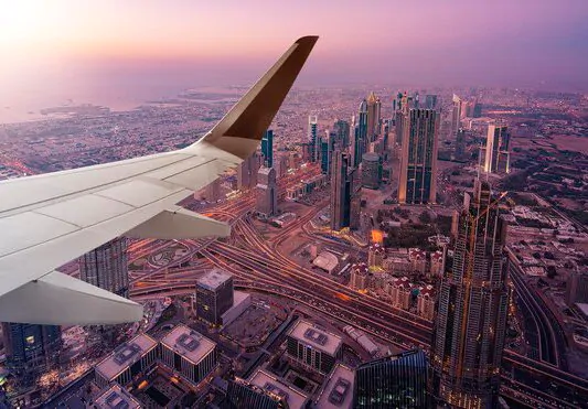 Aerial view from airplane window showing cityscape and airplane wing flying over urban area Airplane wing above city view