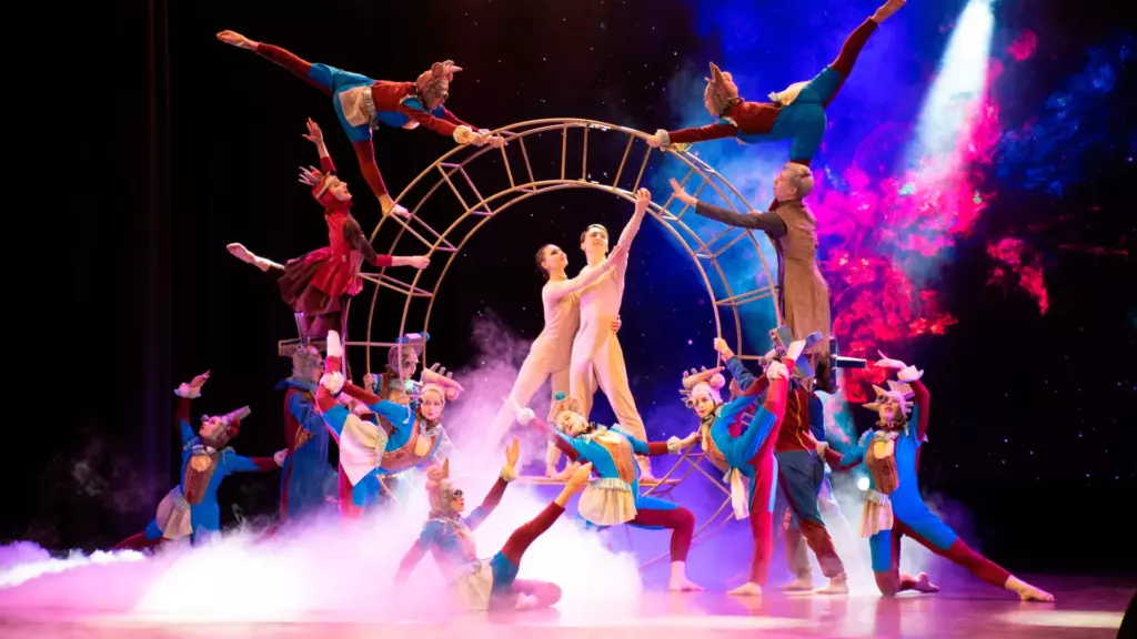 A vibrant dance performance with performers in colorful costumes arranged theatrically around a circular prop Dance performance with performers in colorful costumes